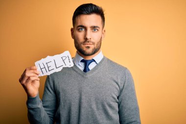 Aşırı çalışan genç iş adamı sarı arka planda kağıt tutarken yardım istiyor. Akıllı bir yüz ifadesiyle ciddi ciddi düşünüyor.
