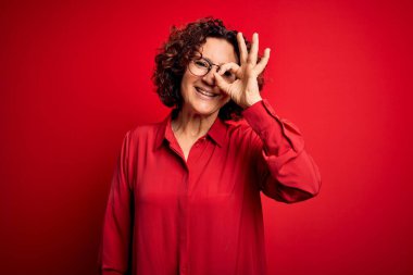Orta yaşlı, kıvırcık saçlı, rahat gömlekli, kırmızı arka planda gözlüklü güzel bir kadın..
