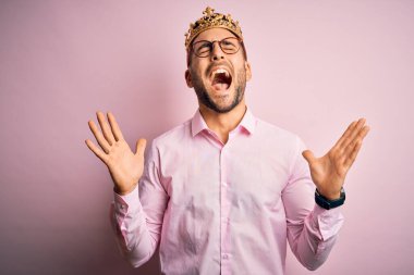 Pembe arka planda altın tacını takmış genç yakışıklı iş adamı kollarını kaldırmış ve gözleri kapalı heyecanla haykırarak başarının çılgınlığını kutluyor. Kazanan konsept