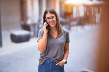 Mutlu ve kendinden emin gülümseyen genç ve güzel bir kadın. Yüzünde gülümsemeyle kasaba caddesinde akıllı telefonun başında konuşmak.