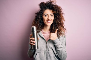 Kıvırcık saçlı, piercingli, termosu olan, mutlu ve gülümseyen genç, güzel bir turist kadın.