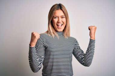 İzole edilmiş arka plan üzerine sıradan çizgili süveter giyen genç, güzel sarışın kadın kollarını kaldırıp açık gözlerle başarının şaşkınlığını ve şaşkınlığını yaşıyor. Kazanan konsept.
