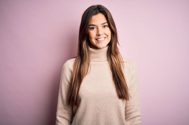 Balıkçı yaka kazak giyen genç ve güzel bir kız izole pembe arka planda mutlu ve havalı bir gülümsemeyle dikiliyor. Şanslı kişi..