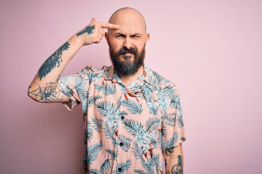 Sakallı, dövmeli, pembe arka planda sıradan bir çiçek gömleği giyen yakışıklı kel adam alnında sivilceyle dolaşmaktan mutsuz, siyah noktalı çirkin bir enfeksiyon olduğunu gösteriyor. Sivilce ve deri problemi