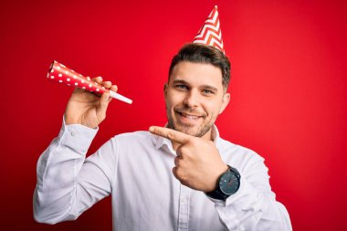 Mavi gözlü genç adam, doğum günü şapkası takıyor ve elinde neşeli bir trompet tutuyor.