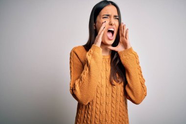 Genç, güzel, esmer bir kadın izole edilmiş beyaz arka plan üzerine günlük süveter giyip elleri ağzında kızgın bir şekilde bağırıyor.