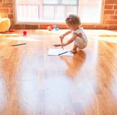 Renkli oyun odasında beyaz güzel bir bebek oyuncaklarla oynuyor. Anaokulunda renkli kalemlerle mutlu ve eğlenceli çizimler..