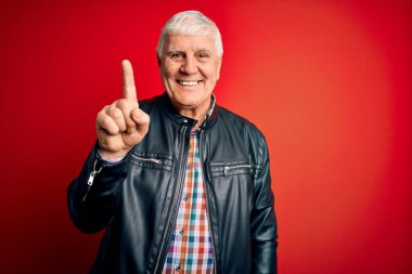 Kıdemli yakışıklı, beyaz gömlekli ve ceketli adam izole edilmiş kırmızı arka plan üzerinde bir numaralı parmağını gösterirken kendine güvenen ve mutlu bir şekilde gülümsüyor..