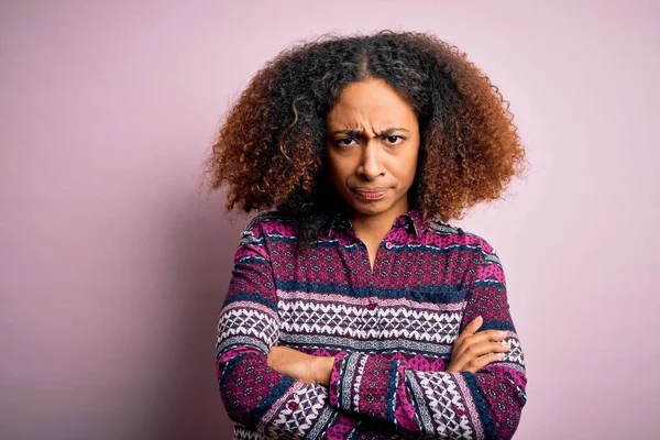 Young african american woman with afro hair wearing colorful shirt over pink background skeptic and nervous, disapproving expression on face with crossed arms. Negative person.