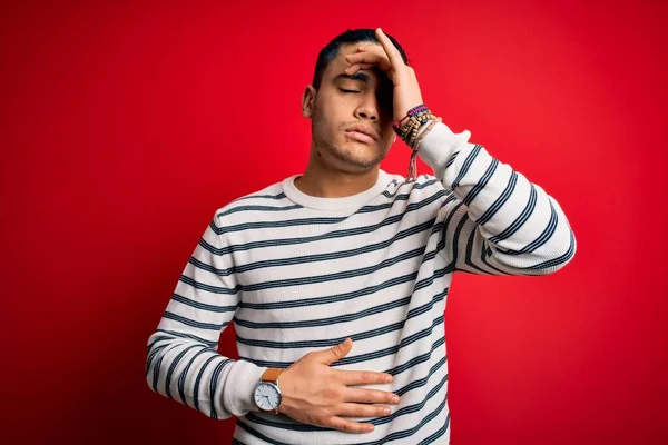 若いブラジル人男性を身に着けているカジュアルストライプTシャツ立って隔離された赤の背景に触れる額病気や熱 インフルエンザや風邪 ウイルス病 — ストック写真