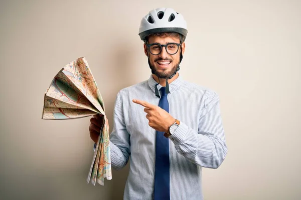 Young businessman wearing glasses and bike helmet holding city map over white bakground very happy pointing with hand and finger