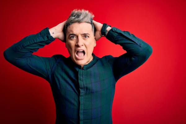 Young handsome modern man wearing elegant green shirt over red isolated background Crazy and scared with hands on head, afraid and surprised of shock with open mouth