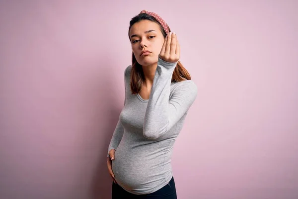 年轻而漂亮的少女怀孕了 她怀着孩子 背负着淡淡的粉色背景 手指手画脚地做着意大利式的手势 — 图库照片