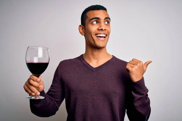白い背景の上に赤ワインのガラスを試飲し 幸せな顔の笑顔で親指で側面まで示すハンサムなアフリカ系アメリカ人ソムリエ — ストック写真