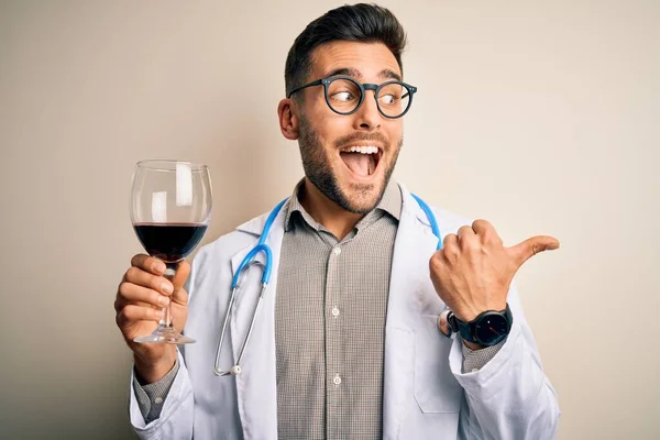 若いです医師男を身に着けています聴診器は 孤立した背景の上に新鮮なワインのガラスを飲みます指すと幸せな顔笑顔で親指で側面まで — ストック写真