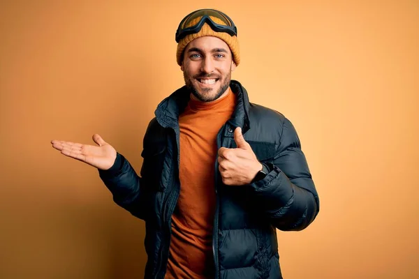 年轻英俊的滑雪者 留着胡子 身穿雪地运动服 戴着滑雪板护目镜 手举着手 竖起大拇指做手势 笑容满面 兴高采烈 — 图库照片