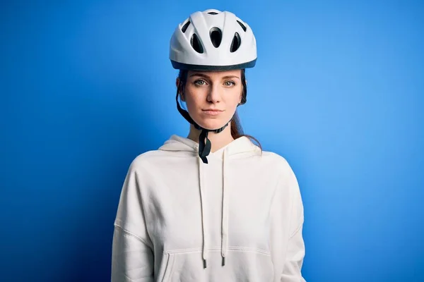 顔に深刻な表現と隔離された青の背景の上に自転車のヘルメットを身に着けている若い美しい赤毛のサイクリストの女性 シンプルで自然なカメラを見て — ストック写真