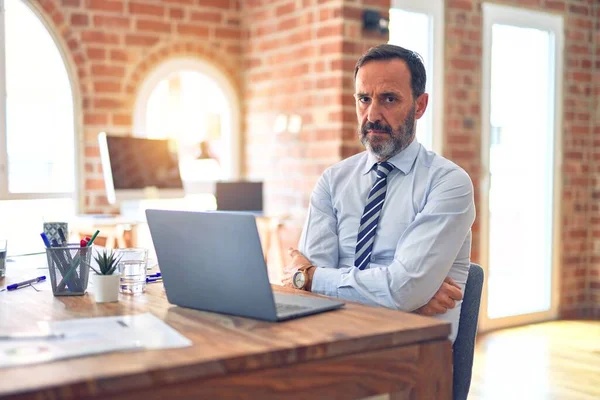 Middle age handsome businessman wearing tie sitting using laptop at the office skeptic and nervous, disapproving expression on face with crossed arms. Negative person.