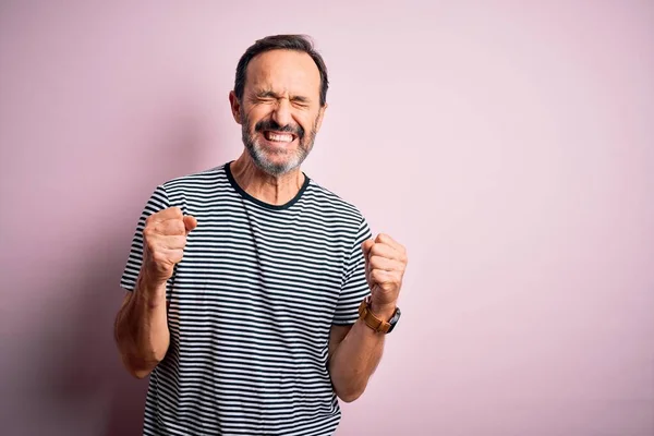 腕を上げ勝利を祝う目を閉じて笑顔で成功のために興奮孤立したピンクの背景の上に立ってカジュアルな縞模様のTシャツを身に着けている中年のホーリーマン 勝者のコンセプト — ストック写真