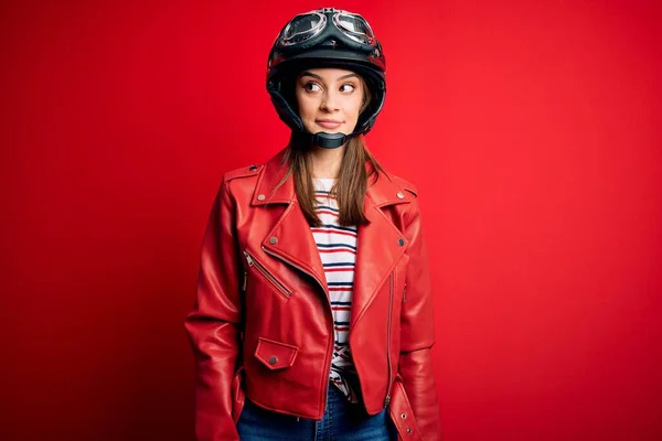 若いです美しいブルネットのオートバイのヘルメットと赤いジャケットを身に着けている女性は横に見て笑って離れて考えて見つめて — ストック写真