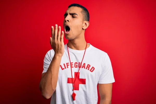 年轻英俊的非洲裔美国救生员 身穿印有红十字和口哨的T恤衫 双手捂着疲惫的嘴打呵欠 感到厌烦 烦躁不安和困倦 — 图库照片