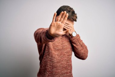 Sakallı ve mavi gözlü genç bir adam beyaz arka plan üzerine günlük süveter giyiyor gözleri ellerle örtüyor ve üzgün ve korku ifadeleriyle jest yapıyor. Utanç verici ve olumsuz bir kavram..