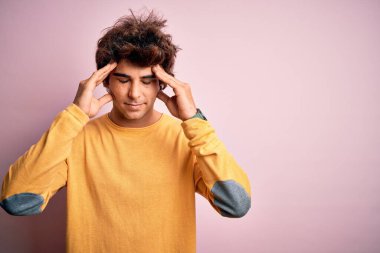 Sarı günlük tişört giyen yakışıklı genç adam, stres yüzünden kafa üstü başı ağrıyan pembe arka plan üzerinde dikiliyor. Migren ağrısı..