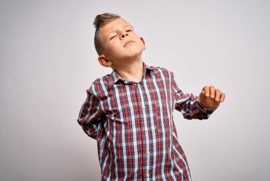 Mavi gözlü, genç beyaz bir çocuk izole edilmiş arka planda duruyor boynu ağrıyor, boynuna elle dokunuyor, kas ağrısı çekiyor.