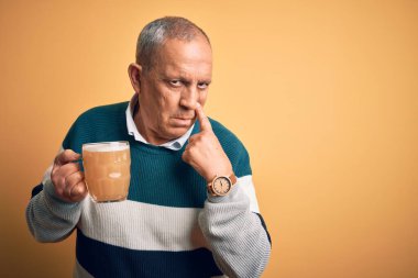 Kıdemli yakışıklı adam, izole edilmiş sarı arka planda duran bira kavanozunu içiyor. Gözlerine işaret ediyor. Hareketlerini izliyor.