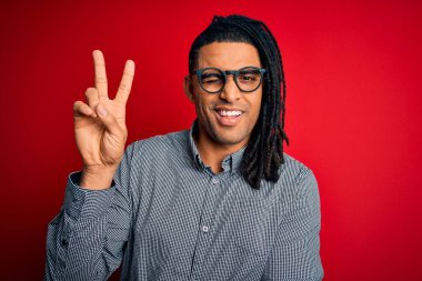 Rastgele gömlek ve gözlük takmış, kameraya gülümseyen ve zafer işareti yapan Afro-Amerikan genç yakışıklı adam. İki numara..