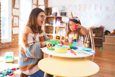 Güzel öğretmen ve çocuk gülümsüyor. Anaokulundaki oyuncakların etrafında plastik yemek ve çatal bıçak kullanarak yemek oynuyorlar.