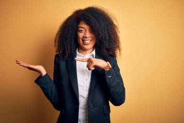 Afro saçlı, zarif ceketli ve kameraya bakıp gülümseyen güzel Afro-Amerikan iş kadını..