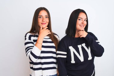 İzole edilmiş beyaz arka plan üzerinde duran sıradan kıyafetler giyen genç ve güzel kadınlar kameraya kollarını kavuşturup gülümseyerek ve çenelerini kaldırarak bakıyorlar. Olumlu düşünüyorum..