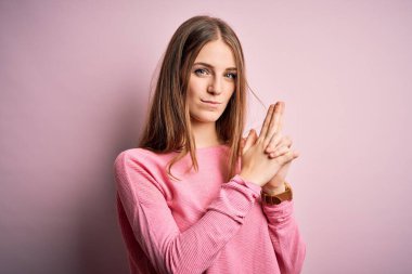 Genç, güzel, kızıl saçlı bir kadın pembe arka plan üzerine günlük süveter giyiyor. Sembolik bir silah tutuyor, el hareketleriyle ateş ediyor, kızgın bir yüz takınıyor.