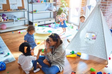 Güzel öğretmen ve bir grup çocuk anaokulunda bir sürü oyuncakla oynuyorlar.
