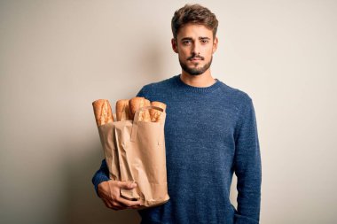 Elinde ekmek dolu kağıt torba tutan genç adam izole edilmiş kırmızı fırının başında duruyor. Akıllı bir yüz ifadesiyle ciddi ciddi düşünüyor.