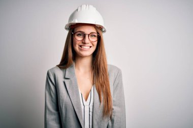 Beyaz arka planda güvenlik kaskı takan güzel, kızıl saçlı, güzel bir mimar kadın. Yüzünde mutlu ve havalı bir gülümseme var. Şanslı kişi..