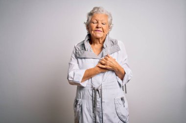 Son sınıf güzeli, gri saçlı, sıradan bir ceket giyen beyaz arka plan üzerinde duran, elleri göğsünde, gözleri kapalı ve yüzünde minnet dolu bir jest olan bir kadın. Sağlık kavramı.
