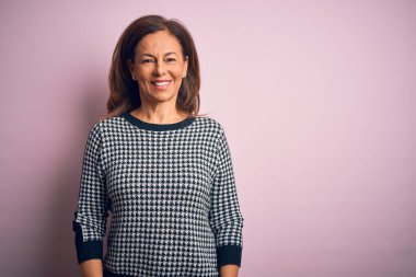 Yüzünde mutlu ve havalı bir gülümseme olan, izole pembe arka planda duran, gündelik süveter giyen orta yaşlı, güzel bir kadın. Şanslı kişi..