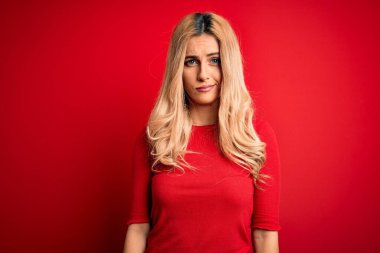 Young beautiful blonde woman wearing casual t-shirt standing over isolated red background skeptic and nervous, frowning upset because of problem. Negative person.