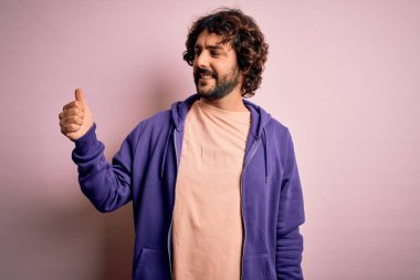 Genç, yakışıklı, sakallı, pembe arka planda sıradan bir kazak giyen gururlu ve gülümseyen bir adam.