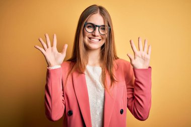 Sarı arka planda ceket ve gözlük takan genç ve güzel kızıl saçlı bir kadın on numaralı parmaklarıyla işaret ederken kendinden emin ve mutlu bir şekilde gülümsüyor..