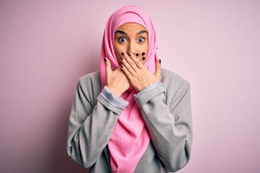 Pembe Müslüman başörtüsü ve iş ceketi giyen genç ve güzel esmer iş kadını yanlışlıkla ağızlarını kapatarak şok etti. Gizli konsept.