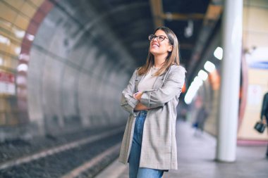 Mutlu ve kendinden emin gülümseyen genç ve güzel bir kadın. Tren istasyonunun peronunda yüzünde gülümsemeyle dikilirken