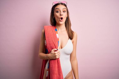Genç ve güzel esmer kadın tatilde. Plaj havlusu ve güneş gözlüğü takıyor. Şok olmuş, korkmuş ve korku ifadesinden heyecanlanmış.