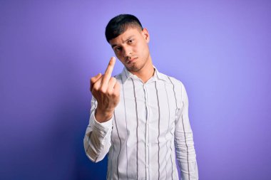 Young handsome hispanic man wearing elegant business shirt standing over purple background Showing middle finger, impolite and rude fuck off expression
