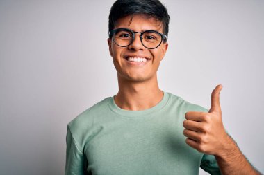 İzole edilmiş beyaz arka plan üzerine gündelik tişört ve gözlük takan genç yakışıklı bir adam mutlu bir el hareketi yapıyor. Kameraya bakıp başarıyı gösteren ifade onaylanıyor.