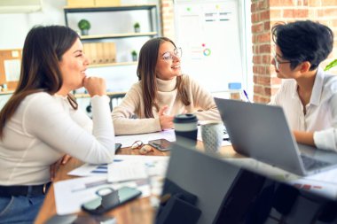 Güzel iş kadınları mutlu gülümsüyor. Gülümseyerek oturup ofiste akıllı telefon ve dizüstü bilgisayar kullanarak çalışmak.