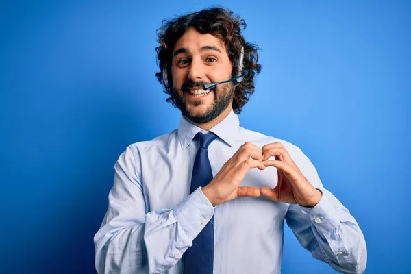 青の背景にヘッドセットを使用して作業ひげを持つ若いハンサムなコールセンターエージェントの男は 愛の心のシンボルと手で形状を示す笑顔 ロマン主義 — ストック写真