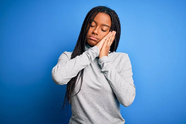 Young african american woman standing wearing casual turtleneck over blue isolated background sleeping tired dreaming and posing with hands together while smiling with closed eyes.